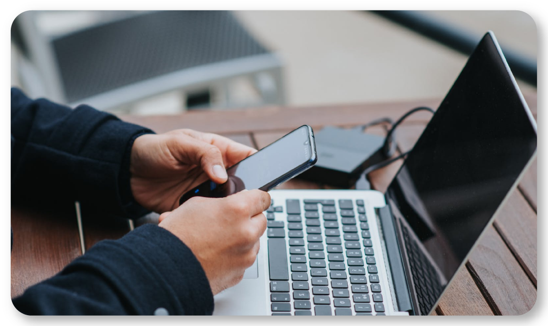 person holding cellphone while looking at their laptop